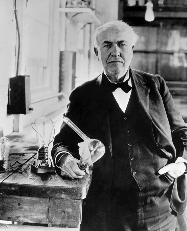 Thomas Edison, 1925, holding a replica of the first electric lightbulb. Publisher Encyclopædia Britannica.
