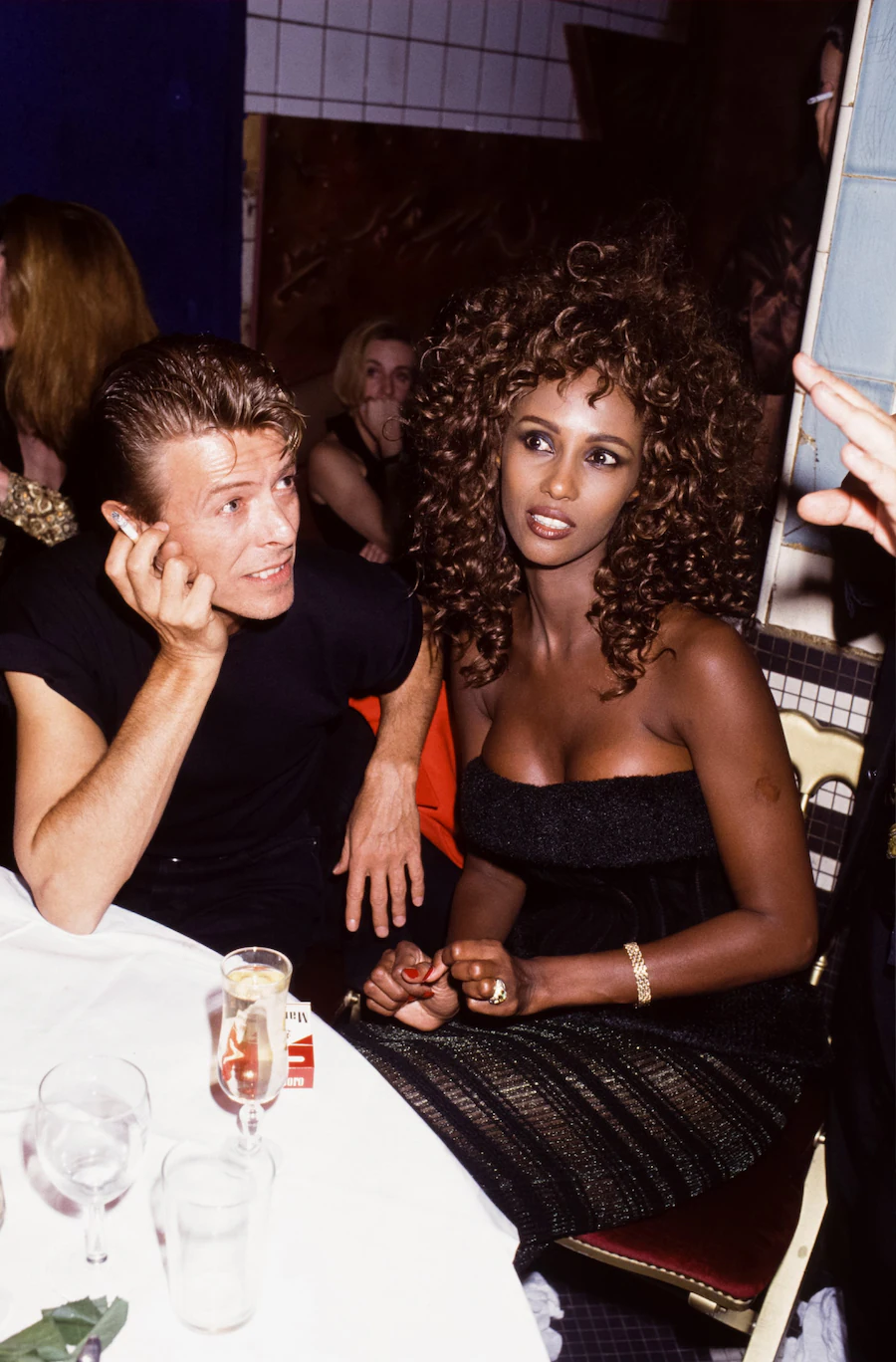 David Bowie and Iman sitting together at a table in Paris, 1991, looking elegant and engaged.